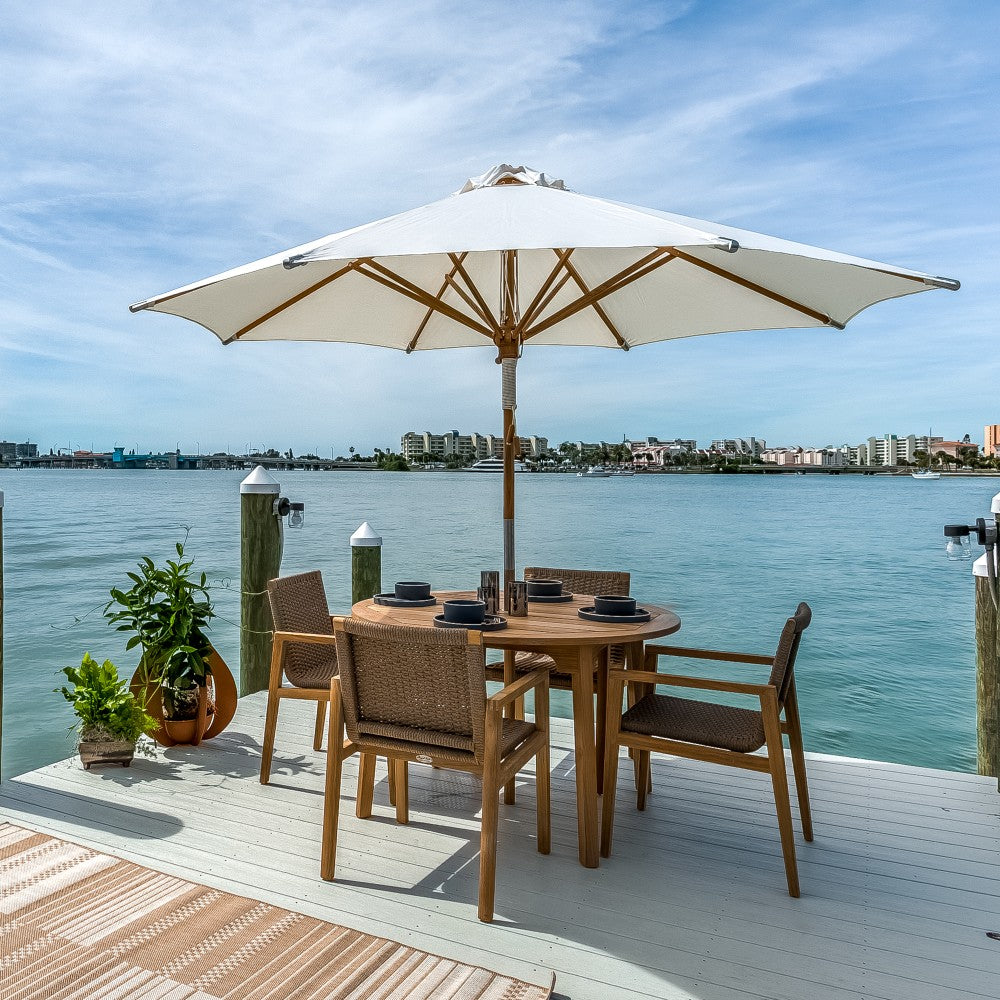 Outdoor dining table set with round teak table, woven chairs, and beige patio umbrella