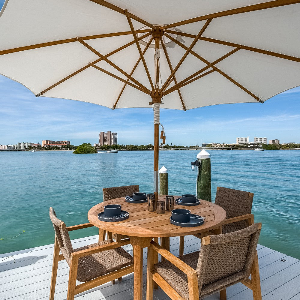 Outdoor round dining table set under a large beige umbrella with woven armchairs