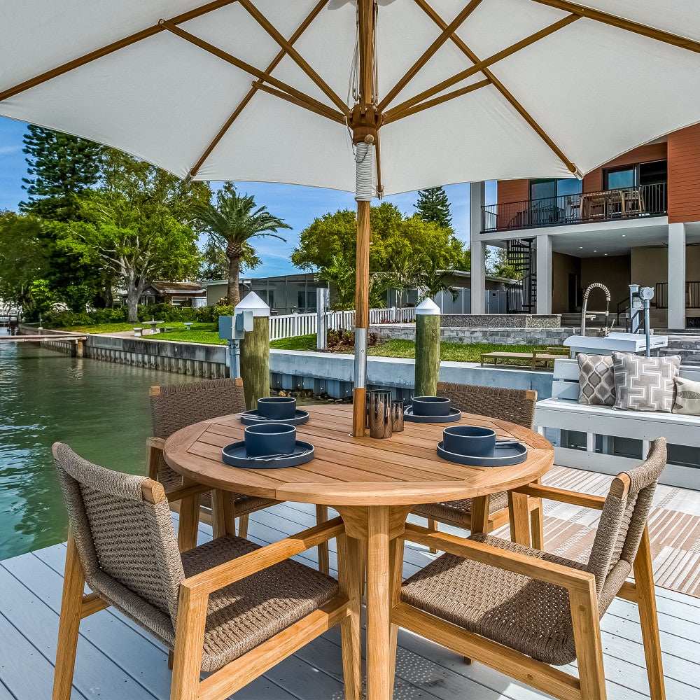 Outdoor dining table set with round teak table and woven chairs under beige umbrella