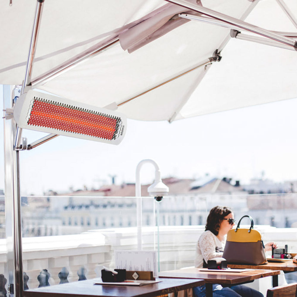 Outdoor hanging electric heater with white housing and red heating element under an umbrella