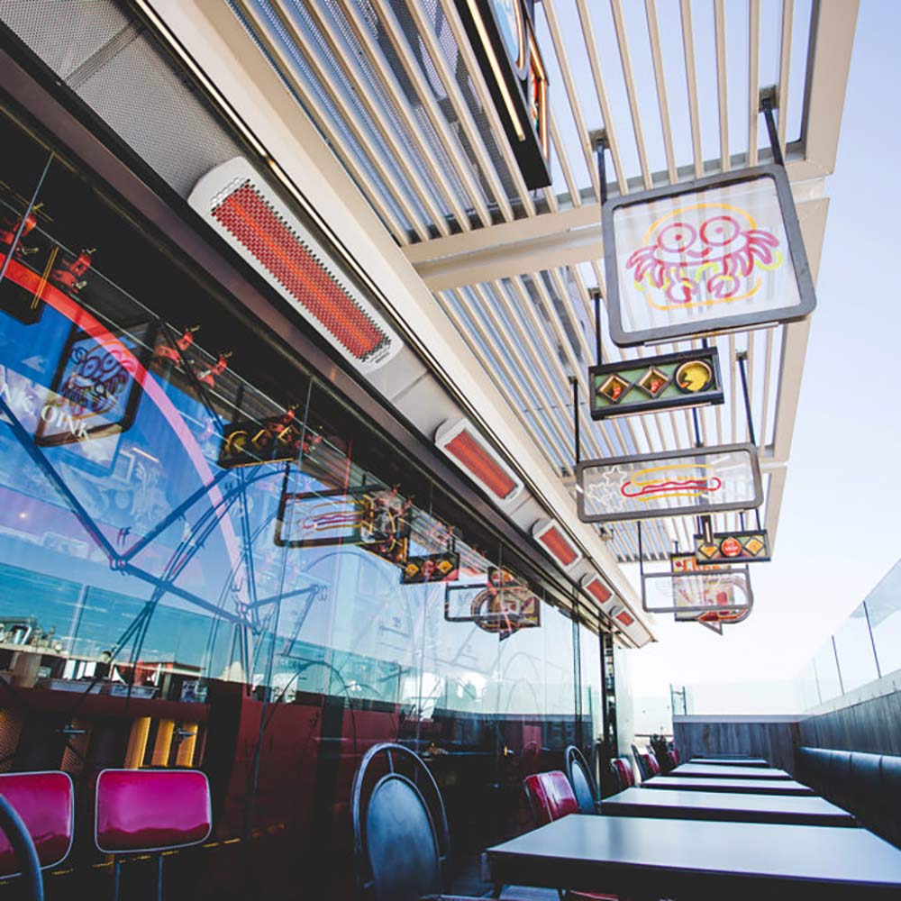 Ceiling-mounted electric heaters with white housings and red heating elements along a glass wall