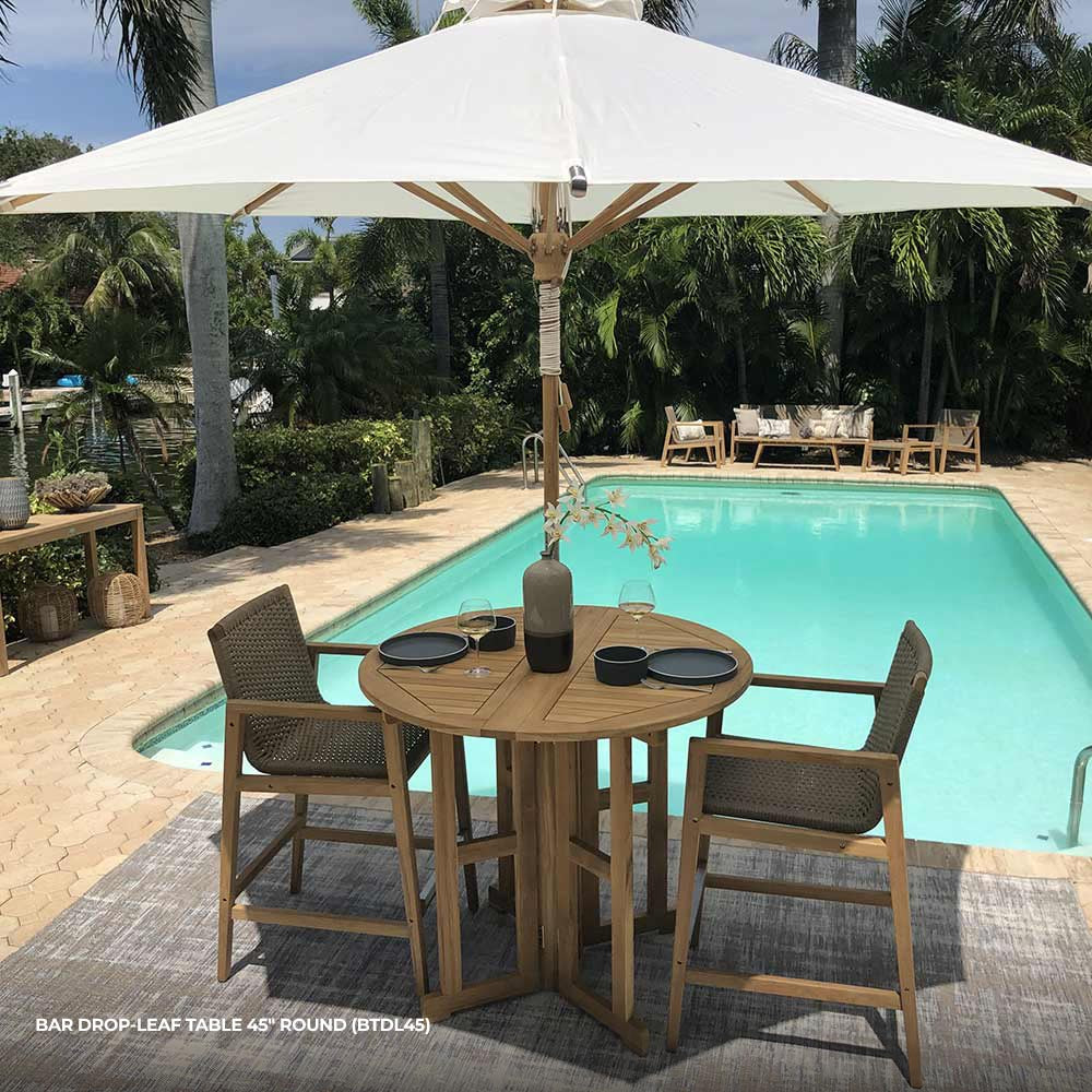 Round teak bar table with slatted drop-leaf top and cross-braced underframe, natural brown.