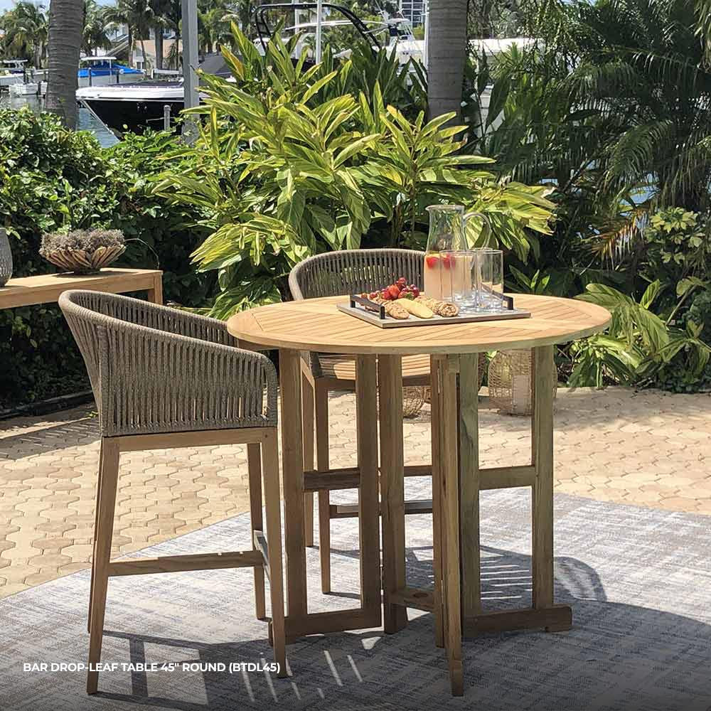 Round teak bar table with slatted drop-leaf top and sturdy legs, natural wood tone.