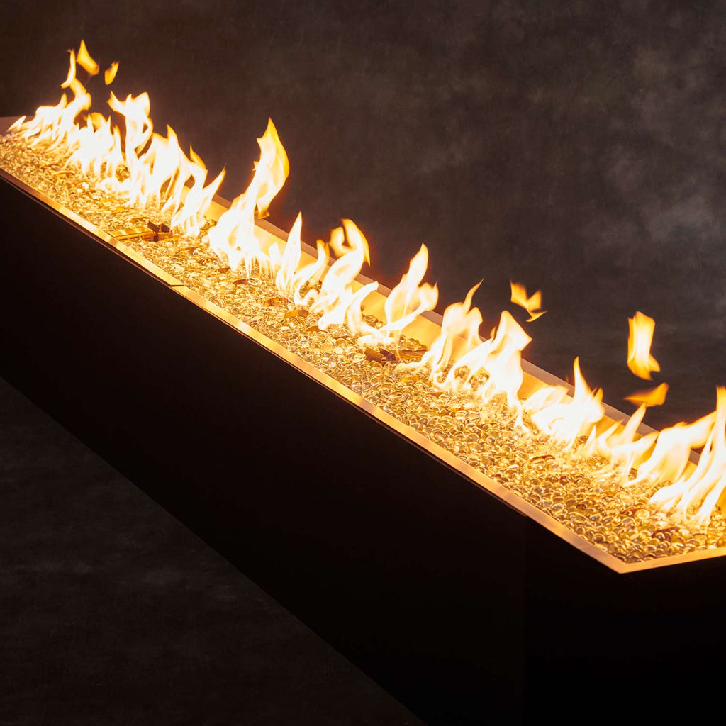 Linear fire pit burner with bright flames across a crystal bed
