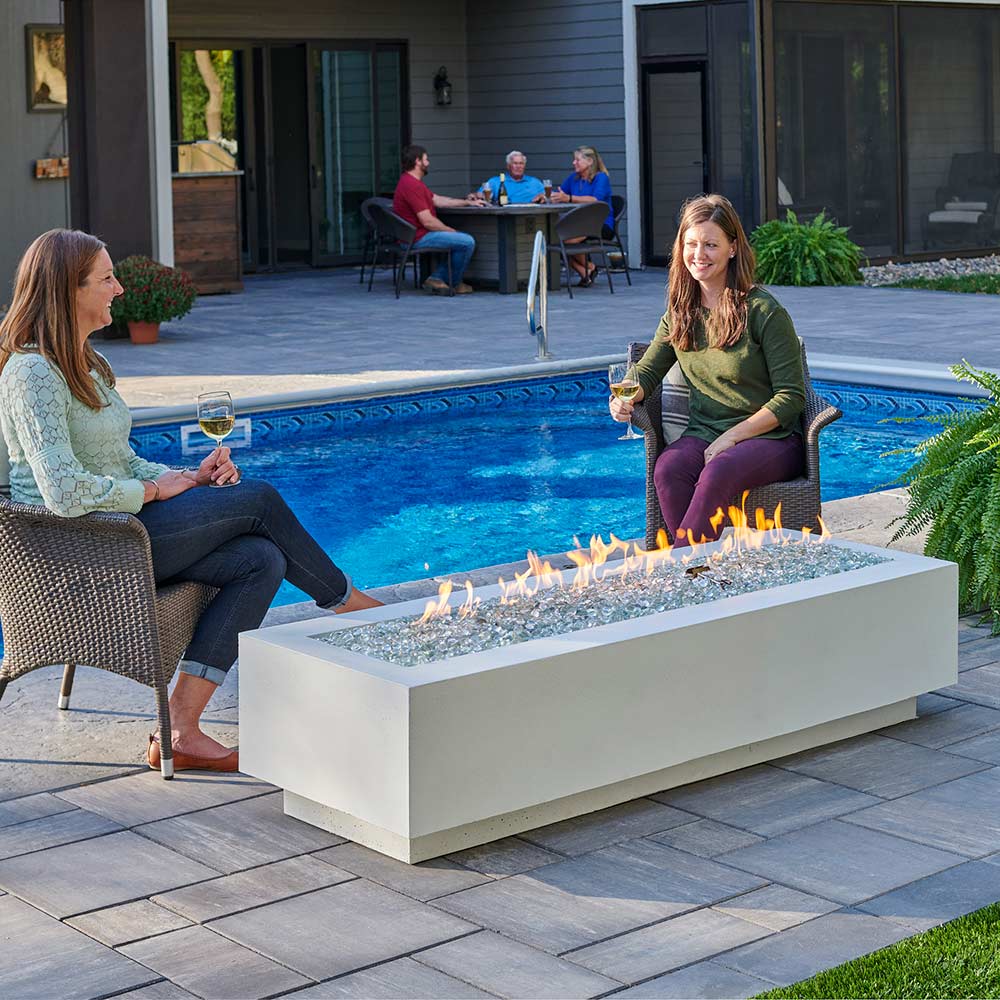 White linear gas fire pit table with flames over glass fire media, outdoor patio setting
