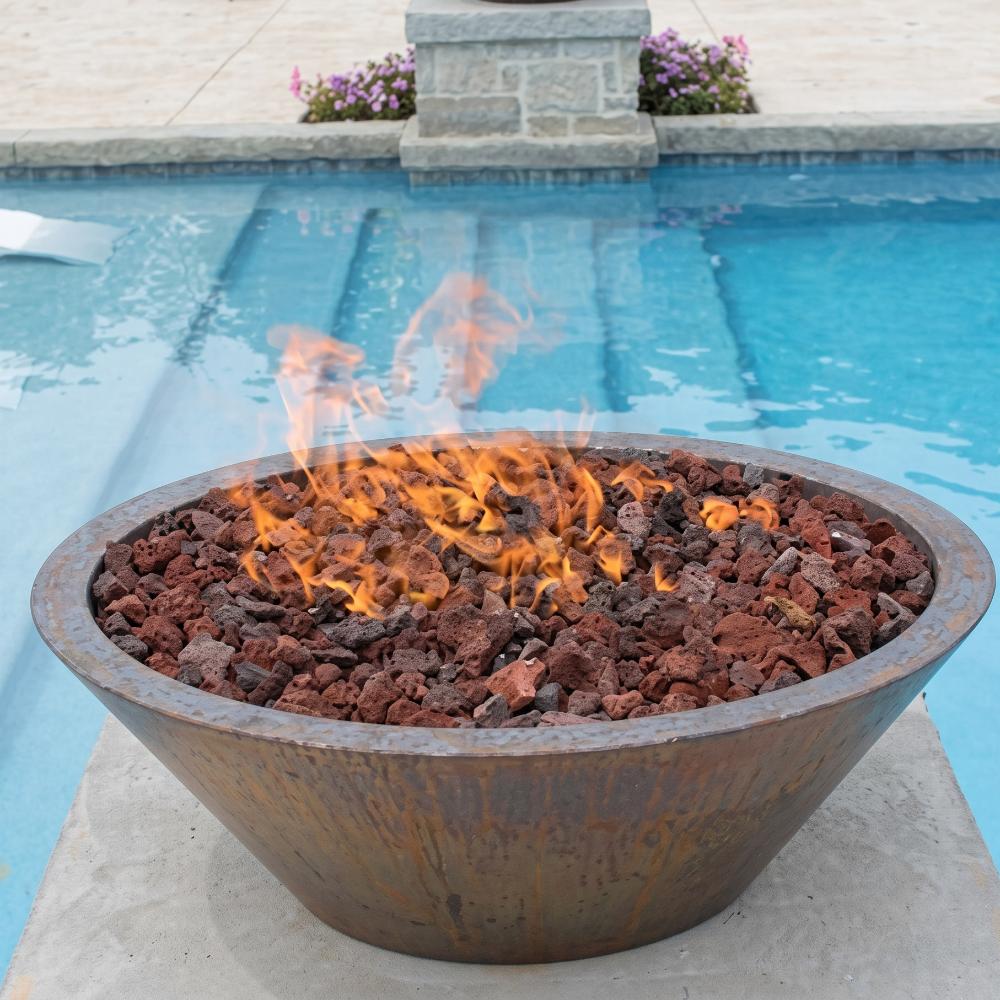 Round hammered copper gas fire bowl filled with lava rocks, orange flames burning