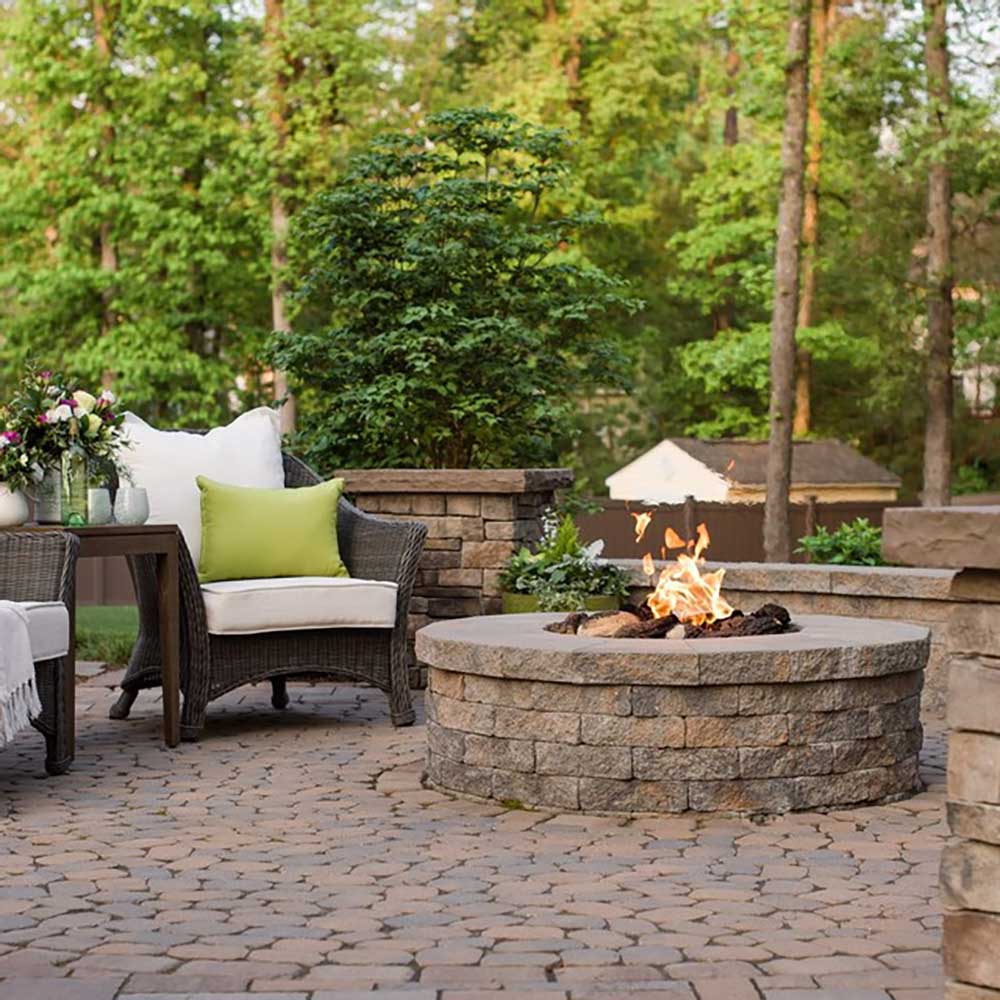 Outdoor gas fire pit burner kit with flame burning inside a stone round fire bowl
