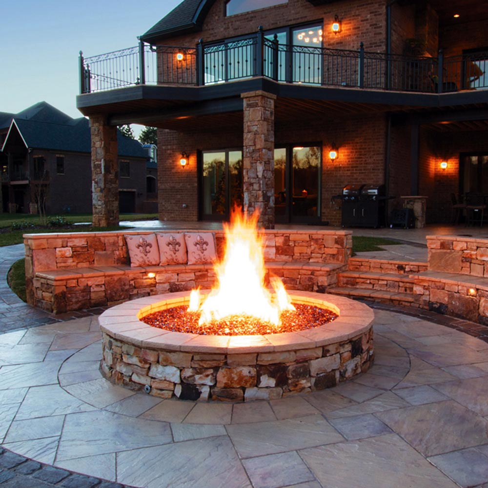 Outdoor stone gas fire pit with prominent central flame and circular burner base