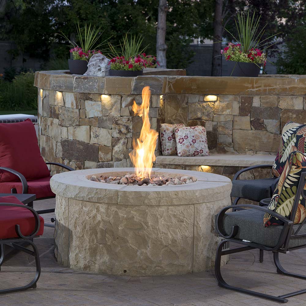 Round stone gas fire pit with tall flame rising from the center burner