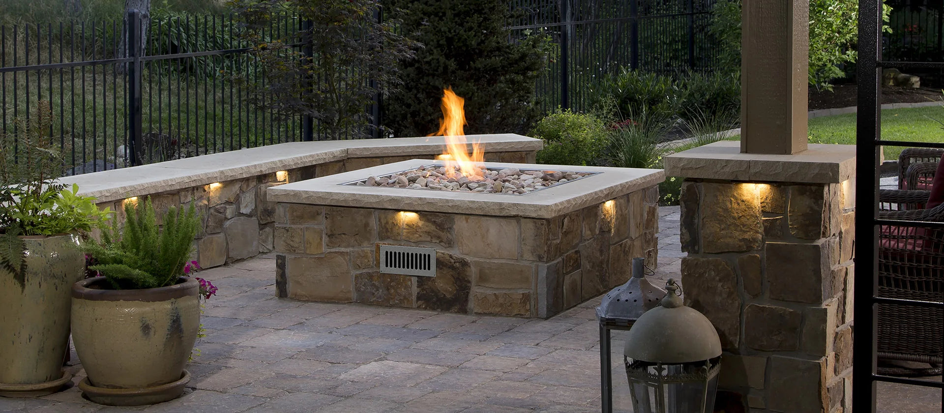 Outdoor patio with stone fire pit, potted plants, and a grill.