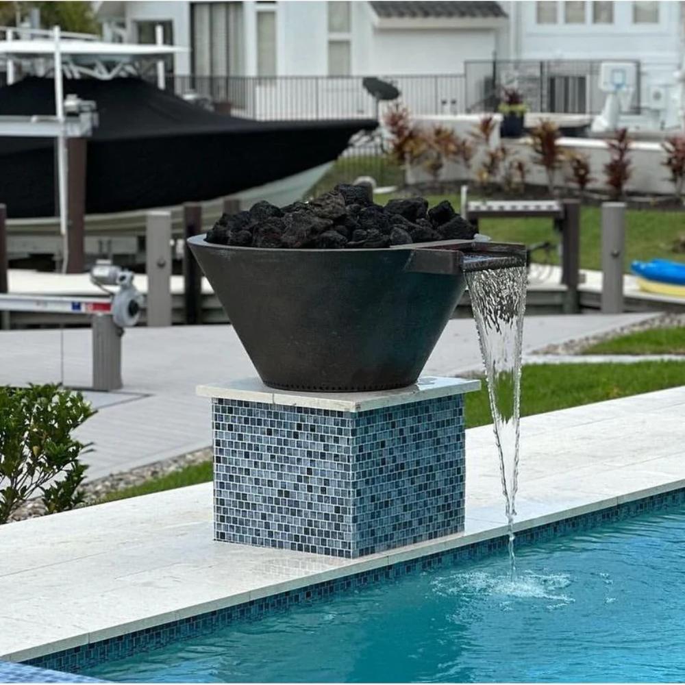 Round gas fire and water bowl with stones and blue mosaic base beside pool water stream.