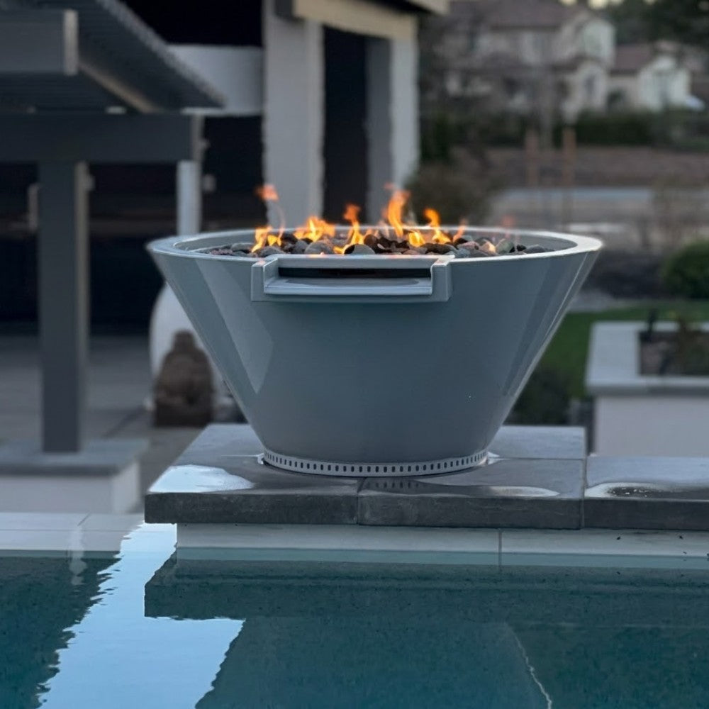 Round gas fire and water bowl with flames, on square stone base at pool edge.
