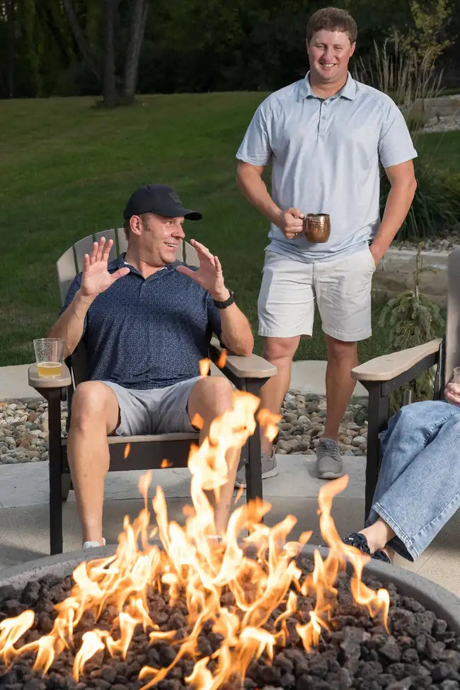 Two men sitting around a fire pit in a backyard setting.