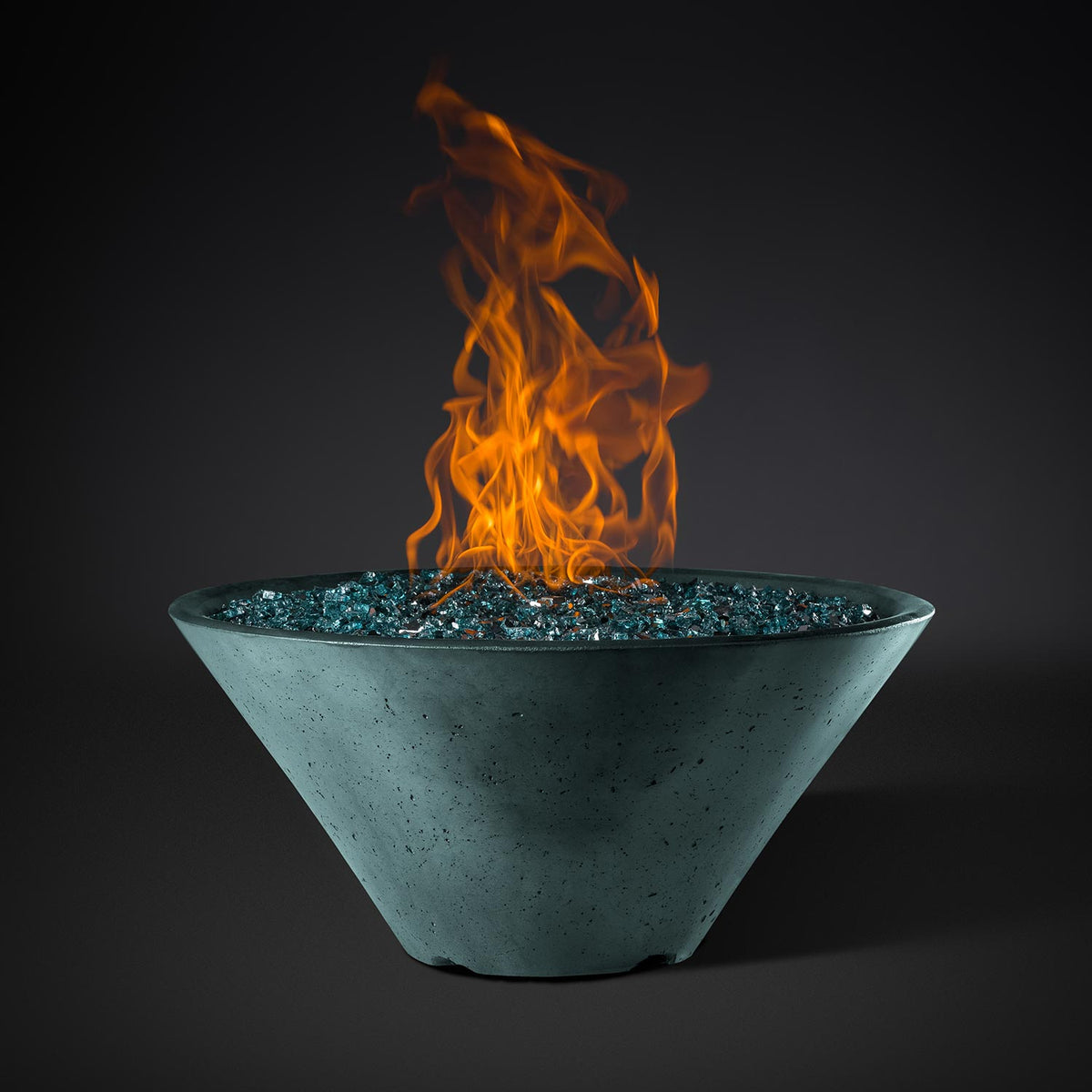 Green round metal fire pit bowl with speckled finish, blue stone bed, and orange flames