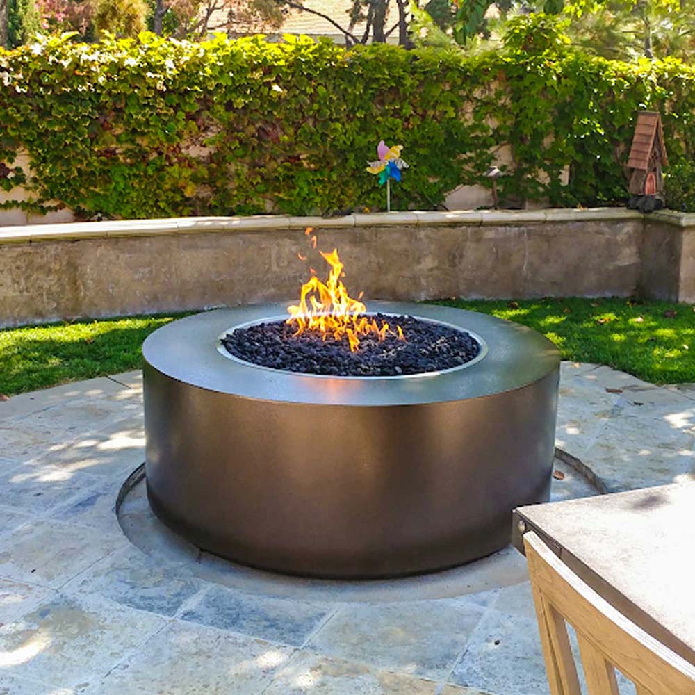 Round gas fire pit with active flame in center bowl on patio