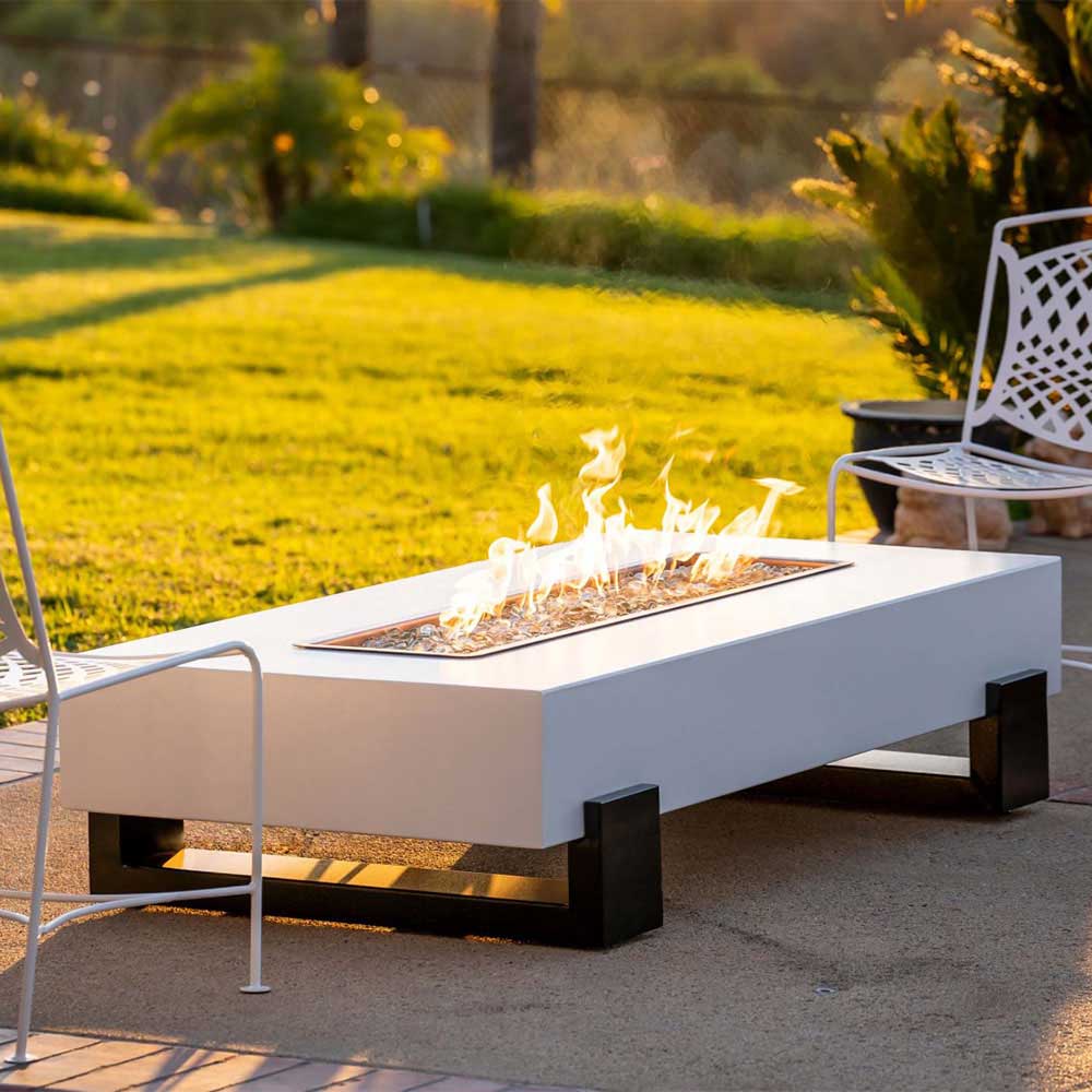 Rectangular gas fire pit on black supports, white surround, burning flames in tray