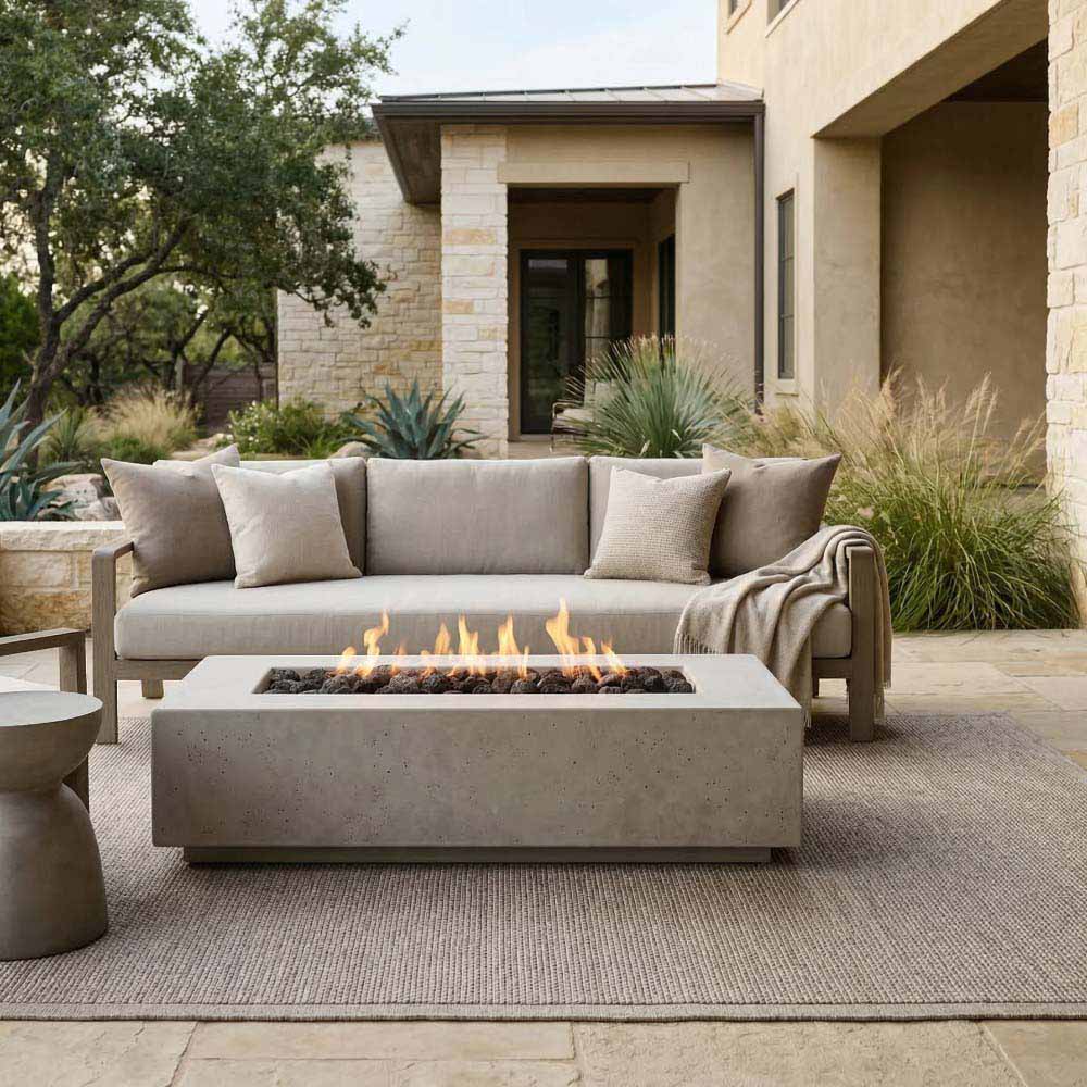 Gray concrete gas fire pit with square burner opening and flames on outdoor patio