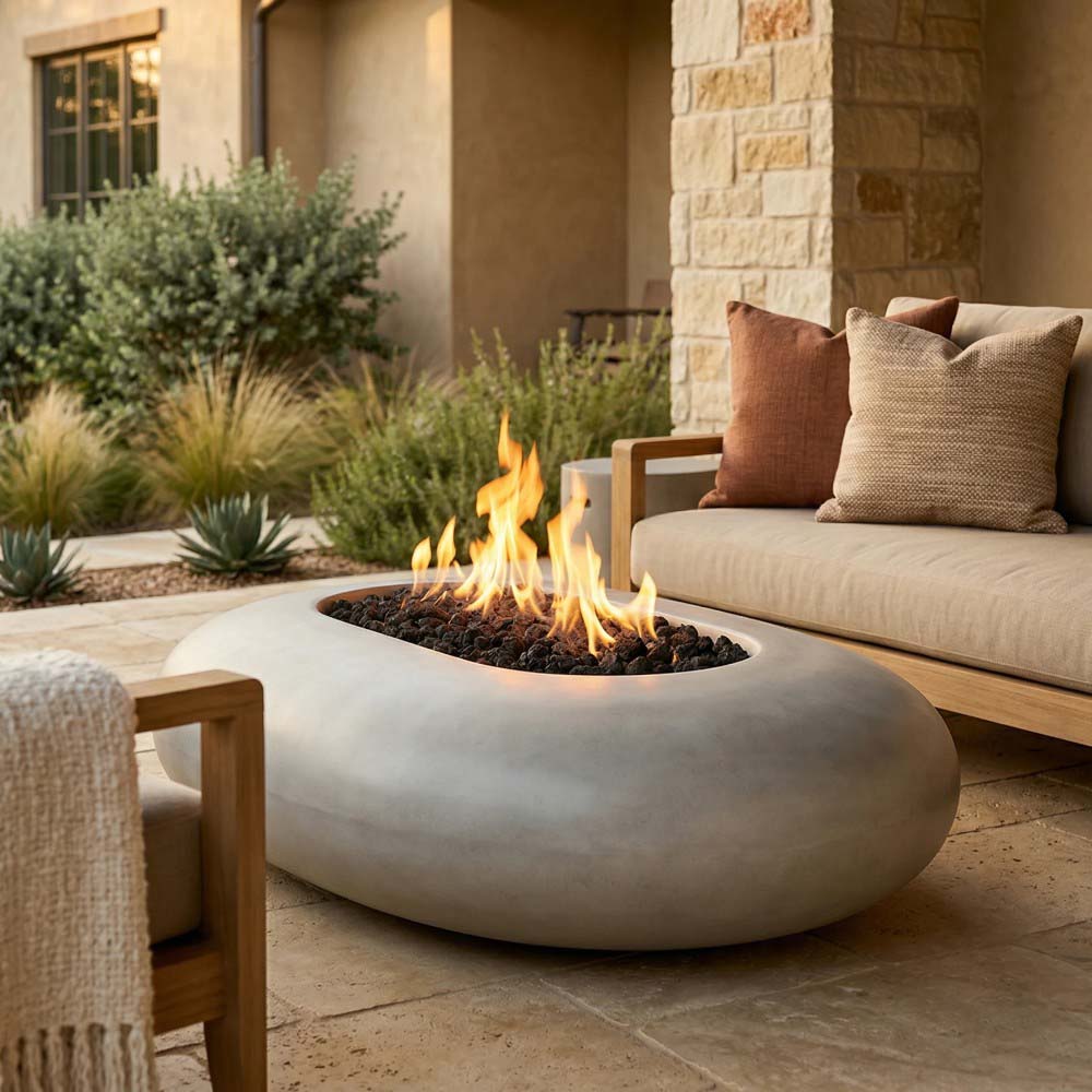 Oval pebble-concrete gas fire pit with burning flames and black rock base
