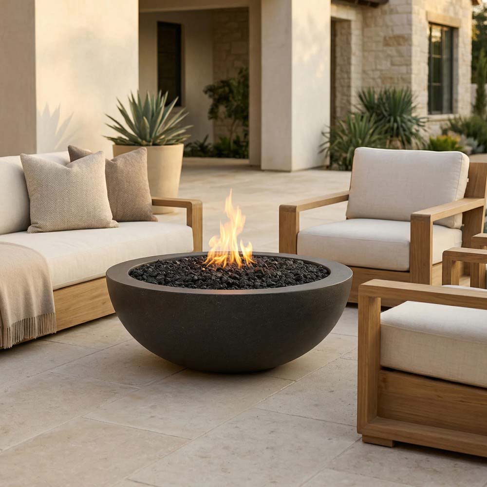 Round concrete gas fire pit with flame center and dark lava rocks on patio