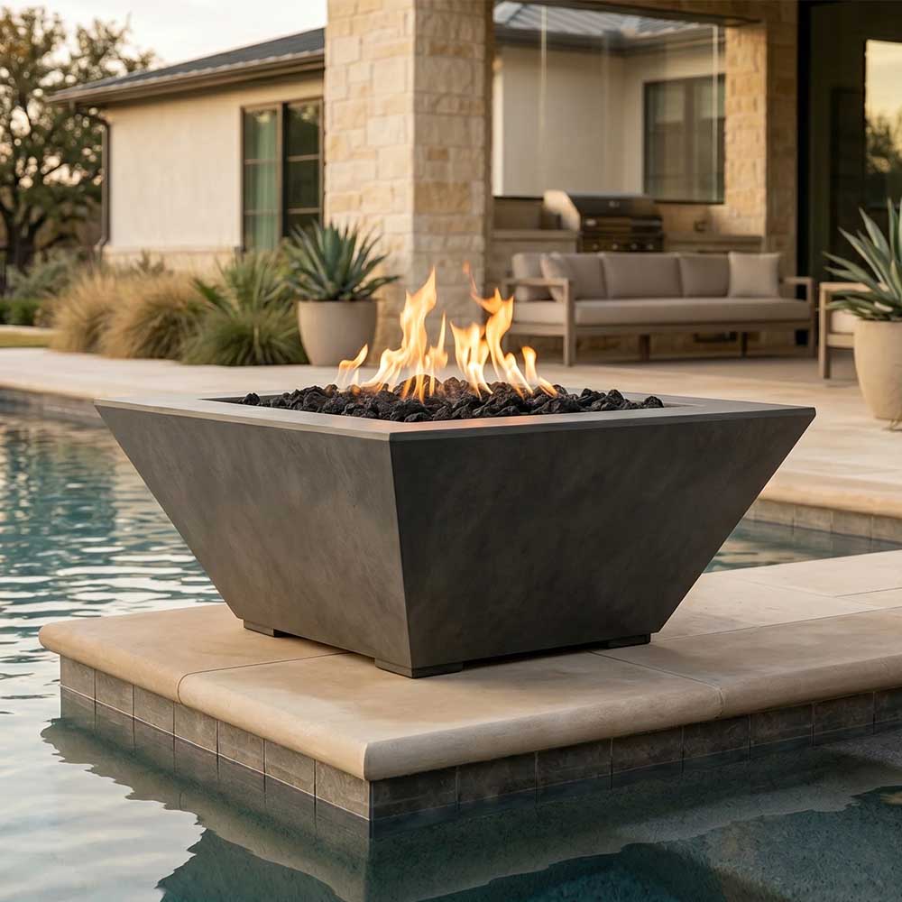 Tall concrete gas fire pit with burning flames and black lava rocks, dark gray finish.