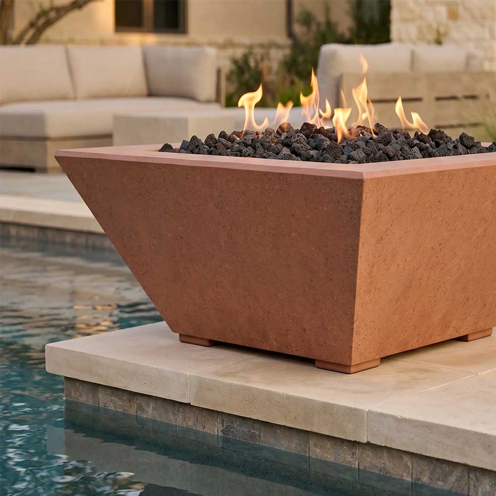 Tall concrete gas fire pit with flames and black lava rocks, brown finish, on patio stone.