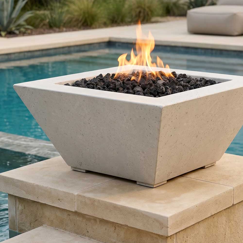 Tall concrete gas fire pit with burning flames and black lava rocks, light beige finish.