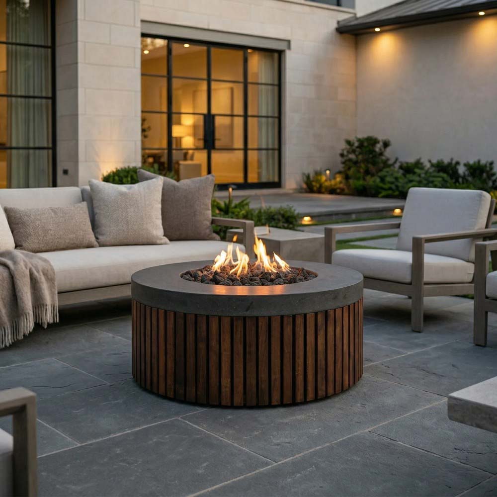 Round outdoor gas fire pit with visible flame and dark wood-slat body on patio