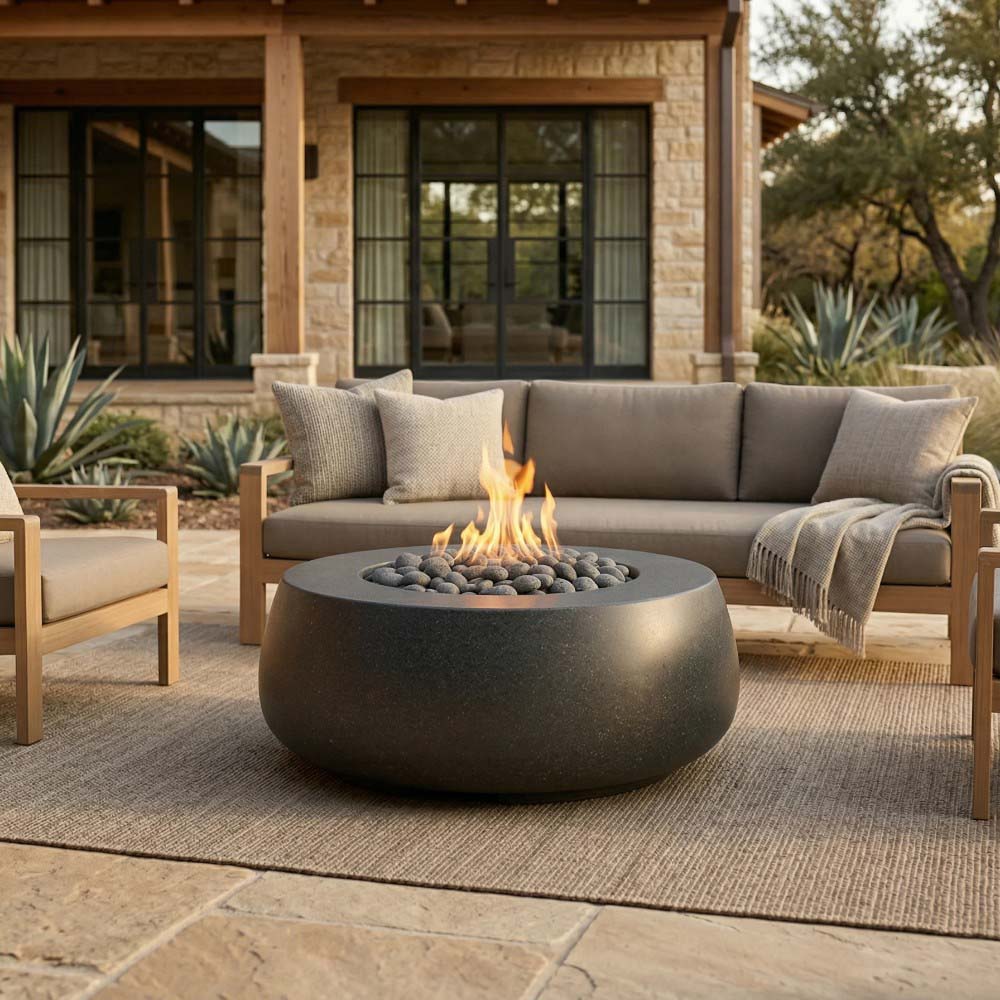 Round dark concrete gas fire bowl with flames over lava rocks on patio