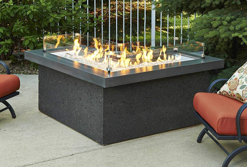 Outdoor fire table with L-shaped clear glass wind guard panels around burner