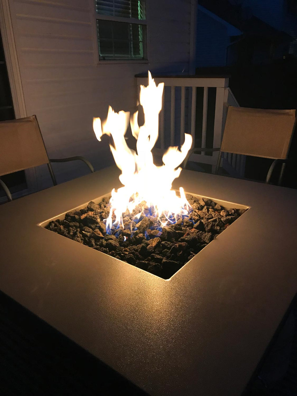 Square gas fire pit with cross-shaped burner and bright flame over rocks