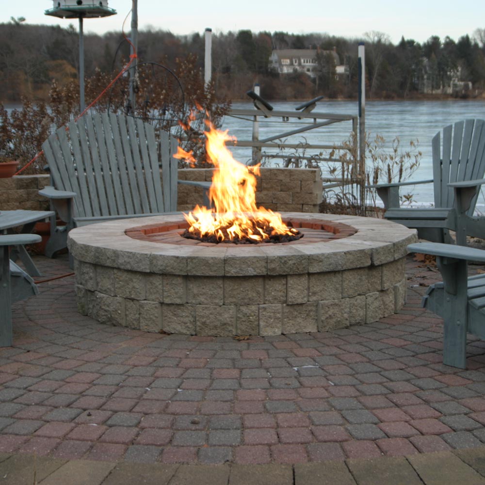 Round stone fire pit bowl with visible flame burning on fire media