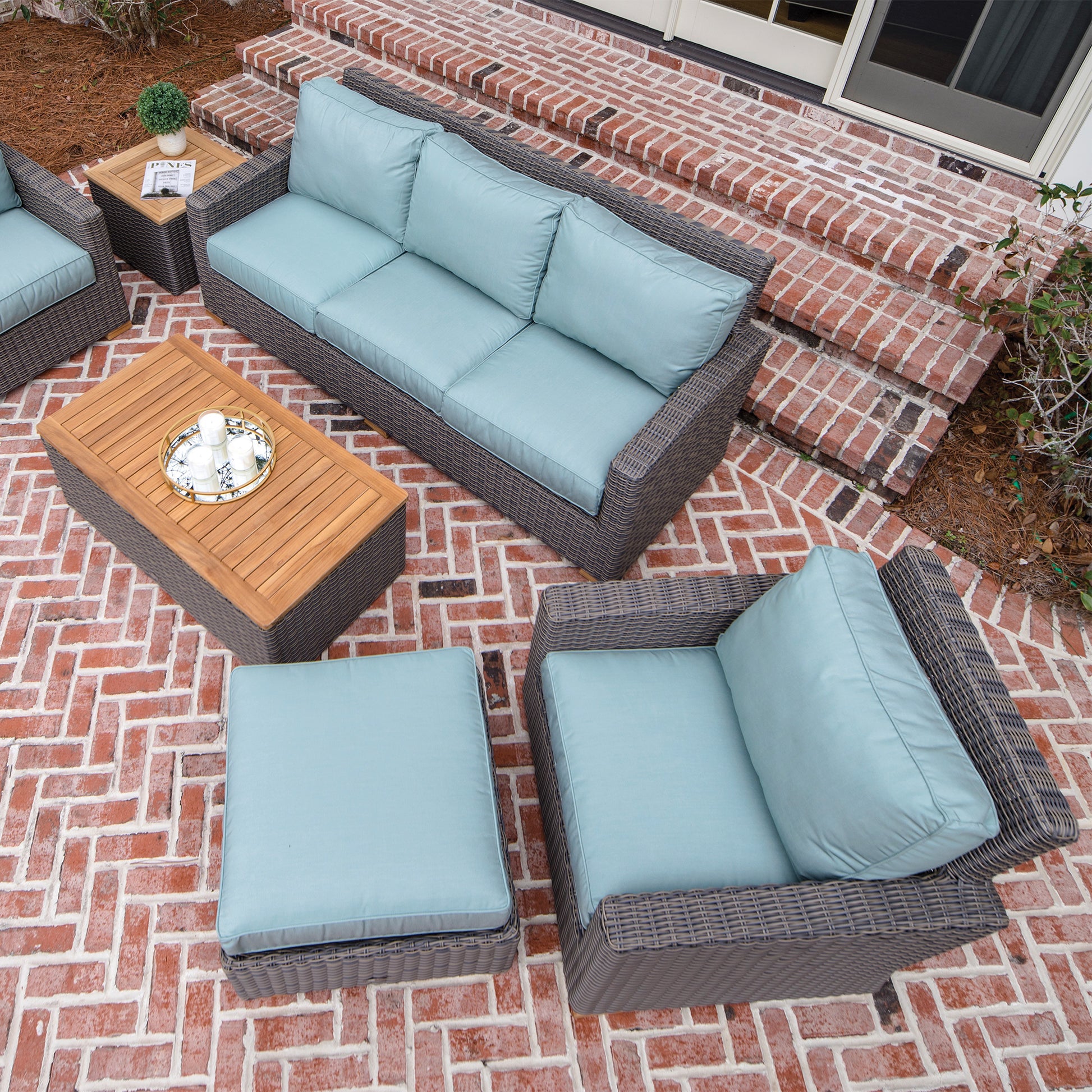 Outdoor sofa set with dark wicker frames and light blue cushions, plus matching ottoman and tables