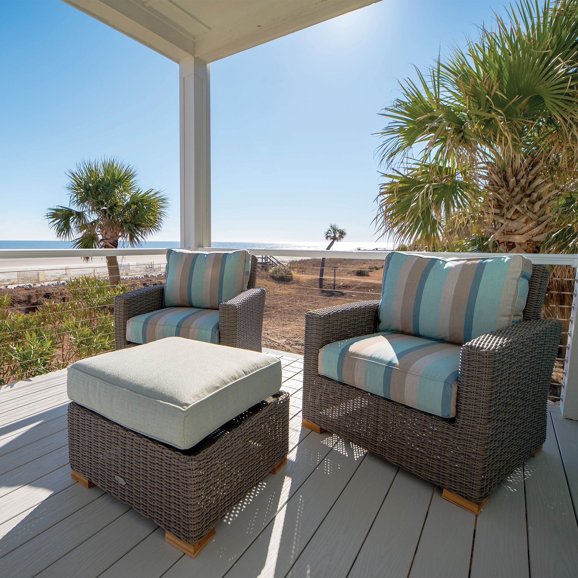 Outdoor seating set with dark wicker armchairs, striped cushions, and a matching ottoman