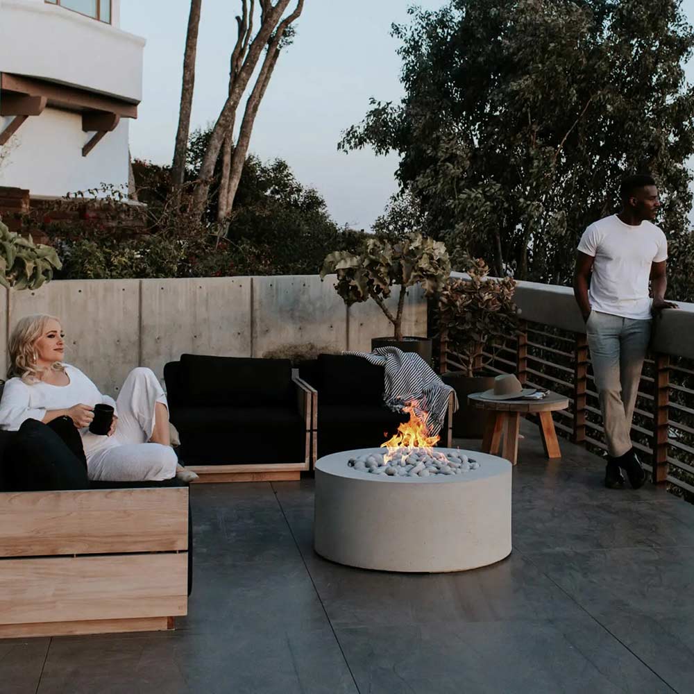 Round lightweight concrete gas fire pit burning with stone-filled bowl