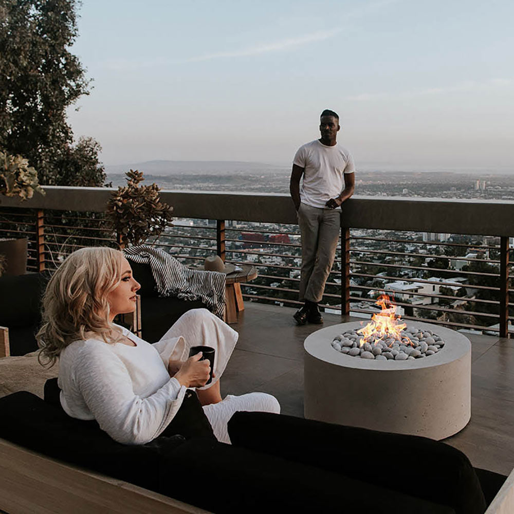 Outdoor round lightweight concrete gas fire pit with flame and grey stones