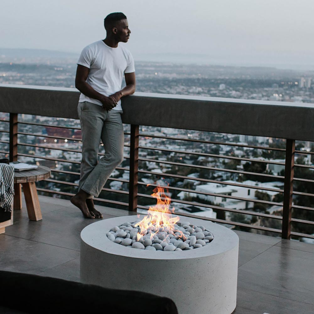 Round lightweight concrete gas fire pit burning with flame and grey stones