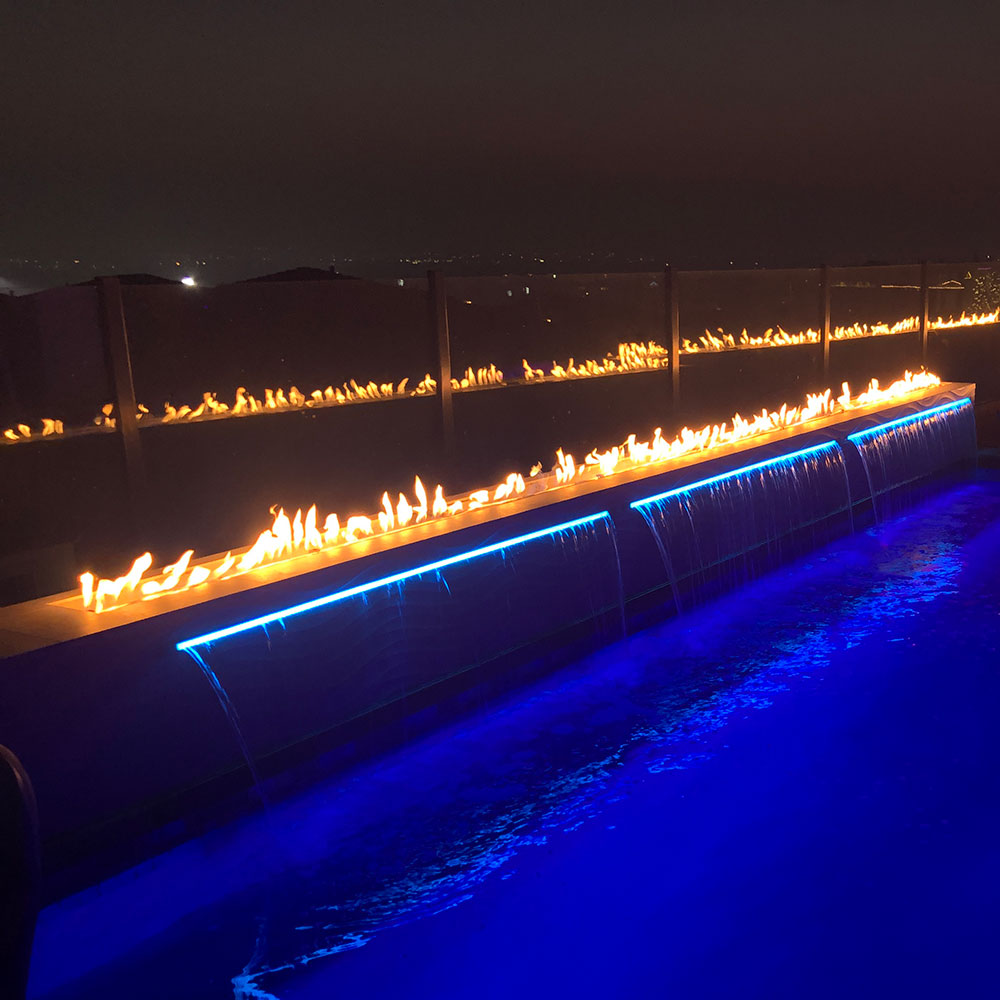 Linear gas fire pit burner with flames along the trough and blue glow under the edge