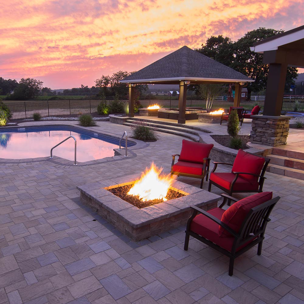 Outdoor gas fire pit with orange flames in a stone burner pan