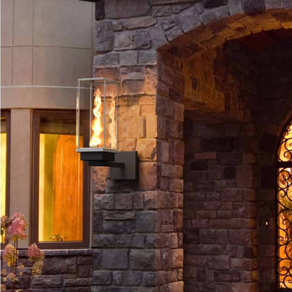 Outdoor wall-mounted gas torch with glass burner and flame on stone wall