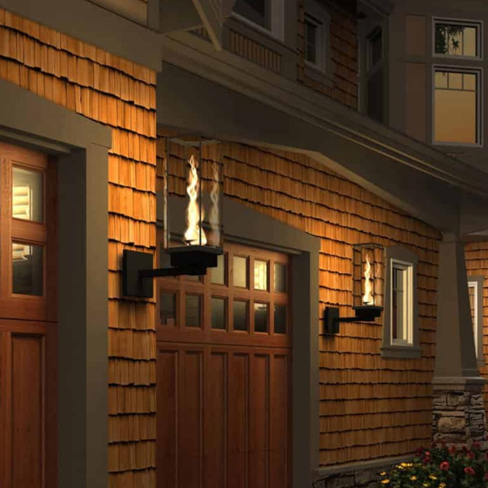 Wall-mounted gas torch with glass enclosure and flame on wood house siding