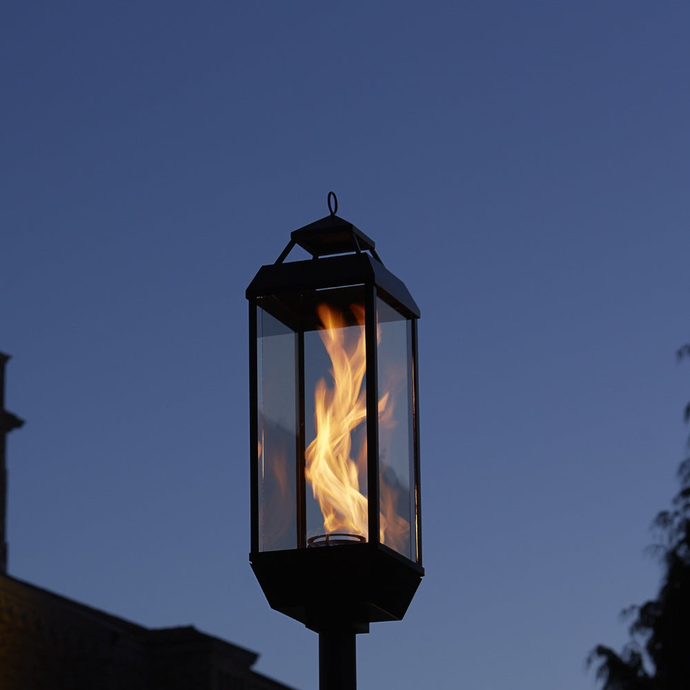 Outdoor gas lantern with tall clear glass panels and blue-black metal, flame centered