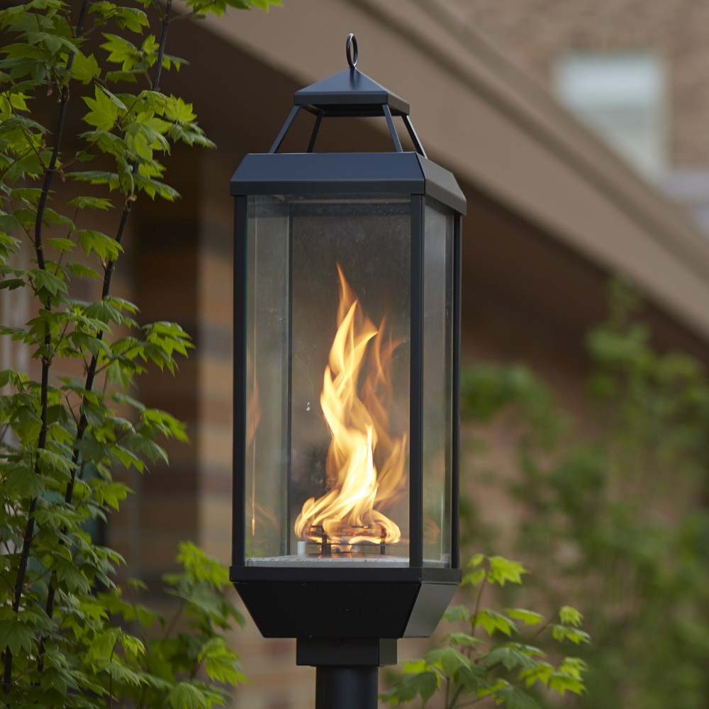 Outdoor gas lantern with dark metal frame, glass panels, and visible flame