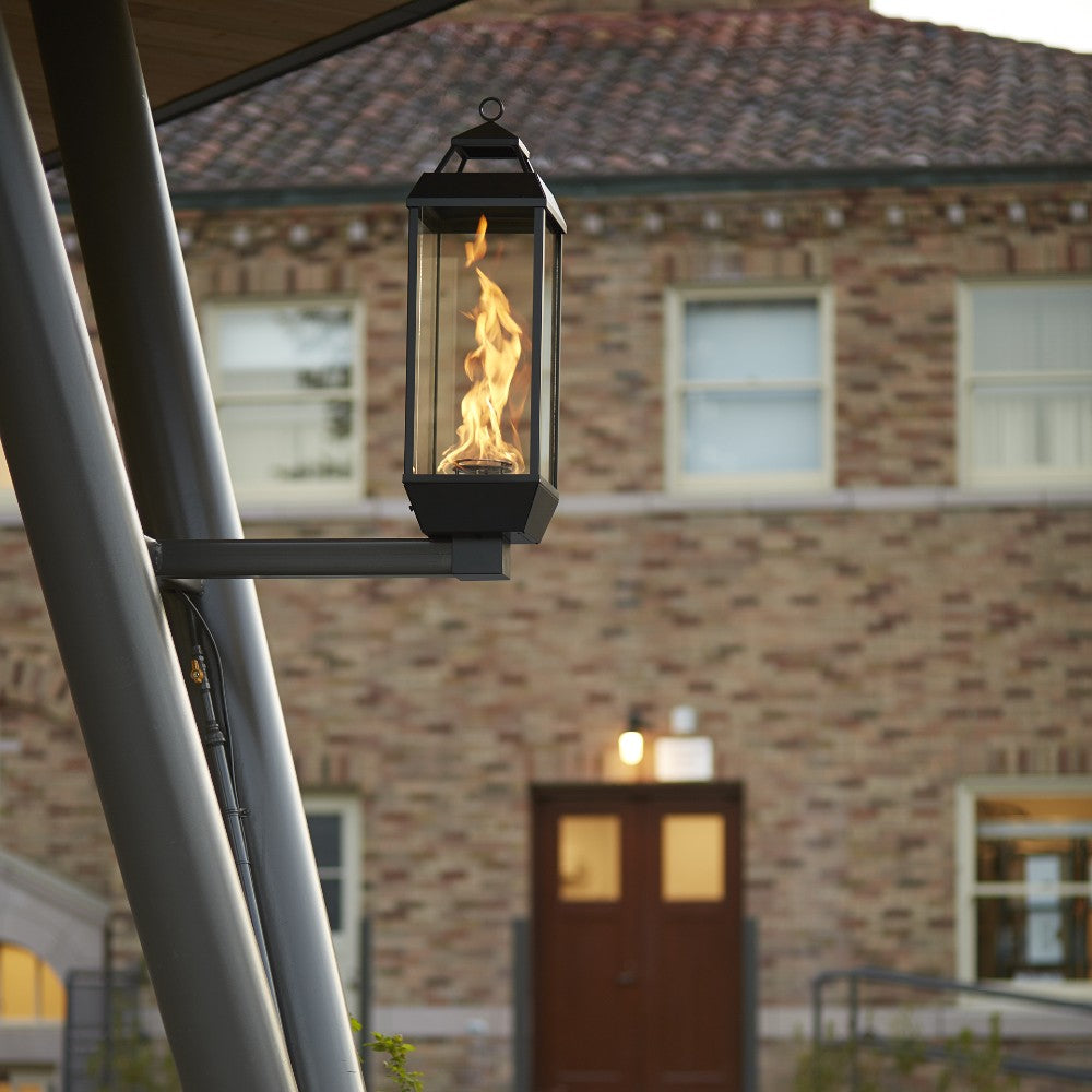 Black gas lantern with glass sides and wall mount bracket, flame burning