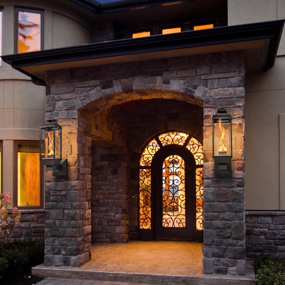 Black gas lantern sconce with glass enclosure and flame on a stone archway