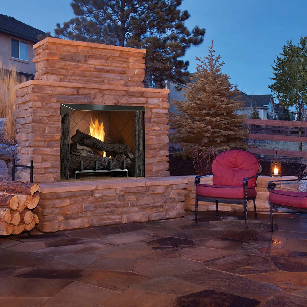 Outdoor gas firebox with stone surround, dark interior, and visible flame behind the grate