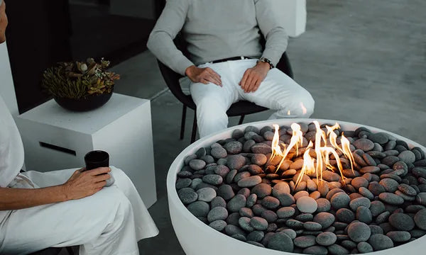 Close-up of a glowing gas fire pit bowl with river rocks and open flames in an upscale outdoor living space