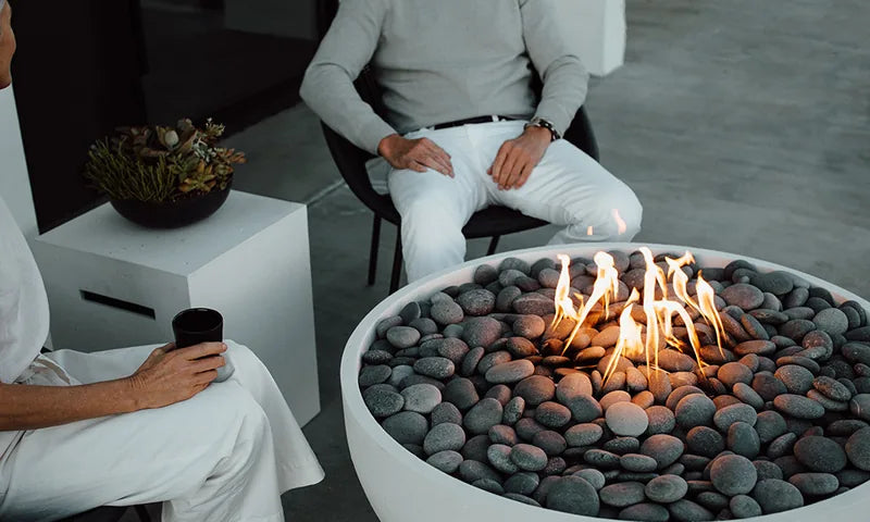 Close-up of a glowing gas fire pit bowl with river rocks and open flames in an upscale outdoor living space