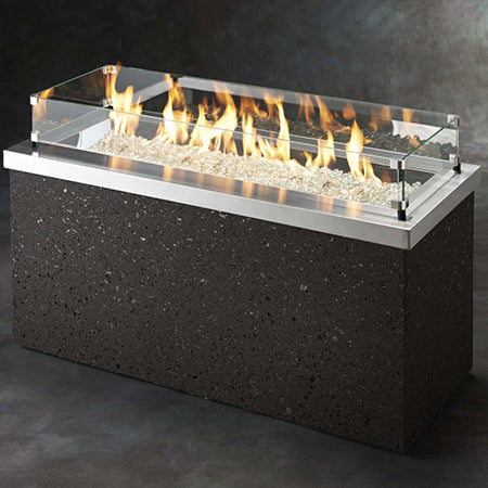Rectangular gas fire pit with stainless frame, glass wind guard, dark stone body, flames