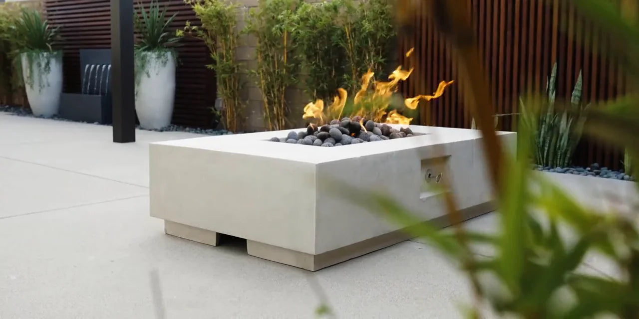 Prism square concrete fire pit with open flame surrounded by lush outdoor landscaping