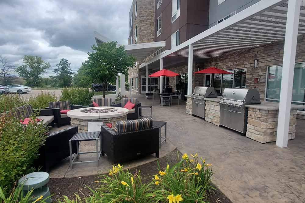 Outdoor patio area with fire pit, chairs, and grills in front of a building.